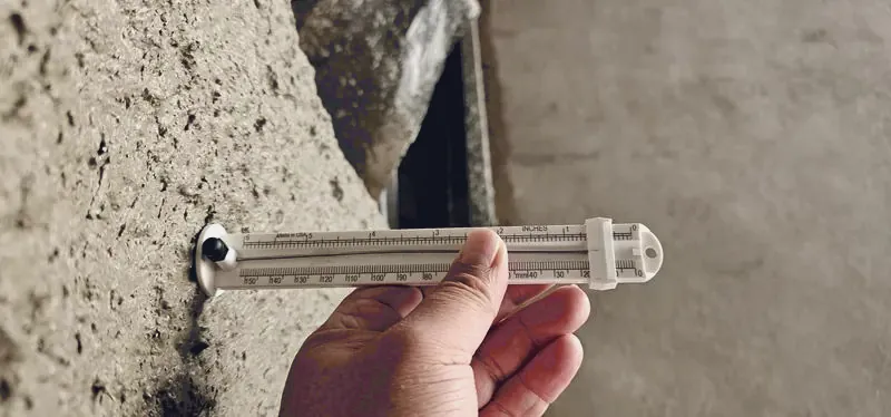 Depth pin gauge held against sprayed cementitious